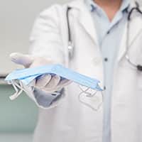 Doctor in a white coat, white gloves holds textile disposable medical masks. epidemic virus outbreak concept